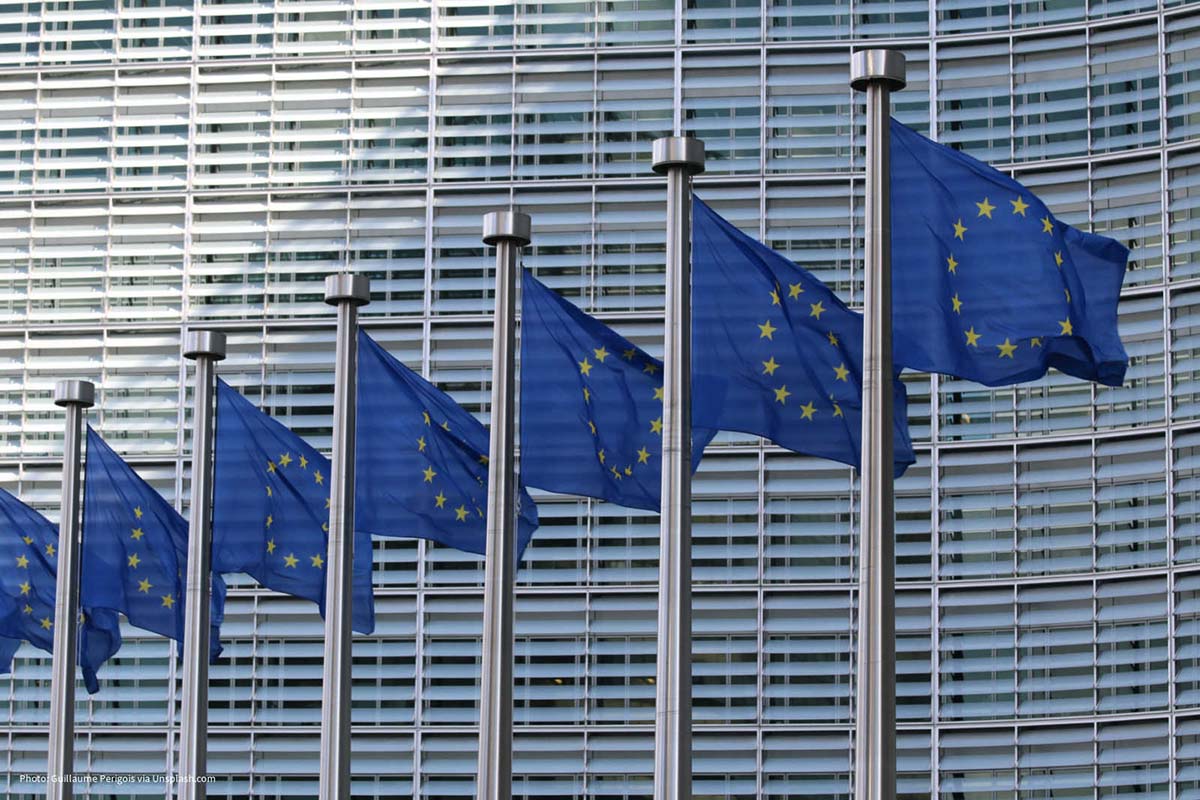 Blue EU flags flying in front of a large building. 