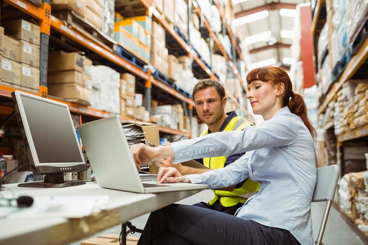 Man and woman in a warehouse looking at a laptop screen.