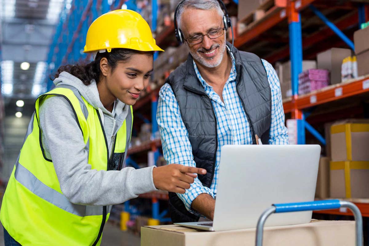 Man and woman in a warehouse looking at a laptop screen.