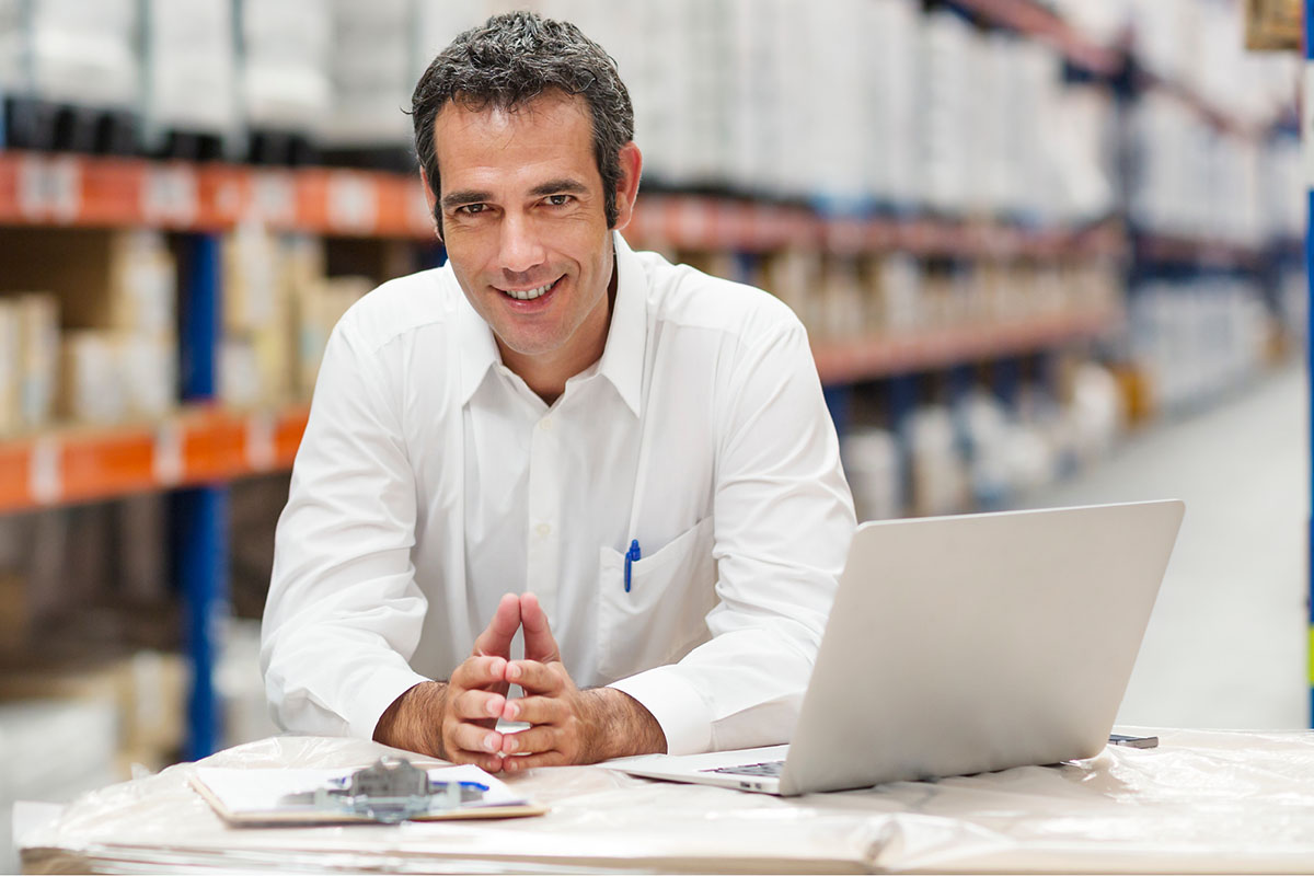 Man in a white shirt sitting at a desk in a warehouse 