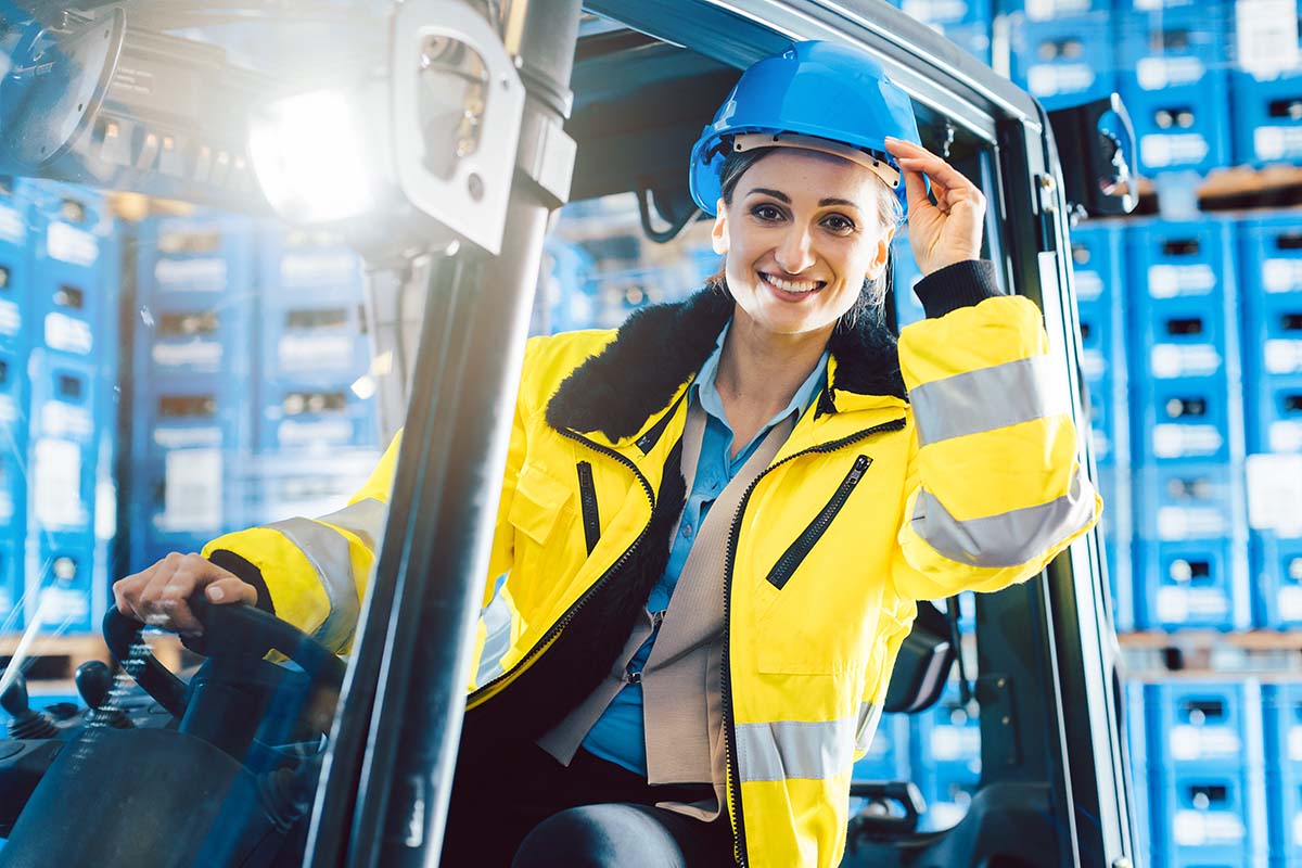 Vrouw op een heftruck met een blauwe veiligheidshelm en een gele jas