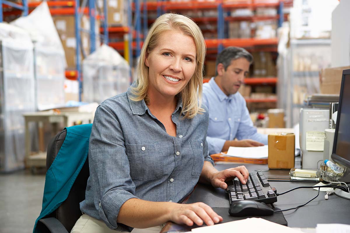 Glimlachende vrouw met computer in magazijn. 