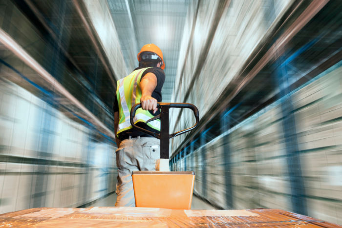 Man pulling a pallet truck in a warehouse with blurred sides indicating movement