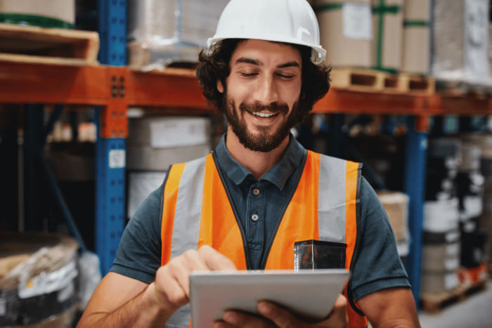 Man met valhelm en oranje vestje in magazijn die werkt op een tablet